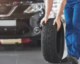 Mecánico con un neumático nuevo, listo para ponerlo en circulación. El coche espera en el taller.