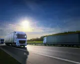 Camiones blancos circulan por la autopista bajo un cielo azul y soleado. El carnet TIR es esencial para estos transportes.