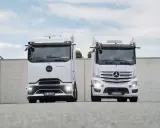 Dos camiones Mercedes-Benz eActros blancos, un nuevo camión eléctrico, se exhiben frente a un muro de hormigón.