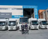 Dos hombres posan frente a una fila de camiones eléctricos de Ontime.
