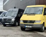 Tres furgonetas Mercedes-Benz Sprinter, una amarilla conmemorativa de 30 años, una negra y una azul, aparcadas frente a un edificio moderno.