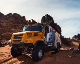 Camión Iveco Dakar amarillo compitiendo en un terreno desértico rocoso y arenoso, levantando polvo.