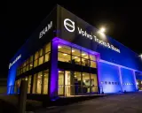 Edificio moderno de EKAM Volvo Trucks & Buses iluminado de noche con luces azules y púrpuras.