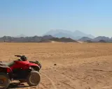 Un quad rojo, listo para la aventura, descansa en el desierto. El carnet para conducir quad 660 es tu pase a la emoción. Montañas distantes y cielo azul completan la escena.