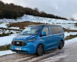 Furgoneta phev azul aparcada en un camino nevado, lista para una aventura invernal.