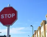 Señal de STOP roja en un poste, con edificios y cielo azul. Indica cómo hacer un stop sin visibilidad.