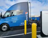 Camión semirremolque azul Pepsi junto a un cargador Tesla.