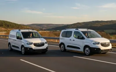 Dos furgonetas panel blancas circulan por una carretera con colinas boscosas al fondo.