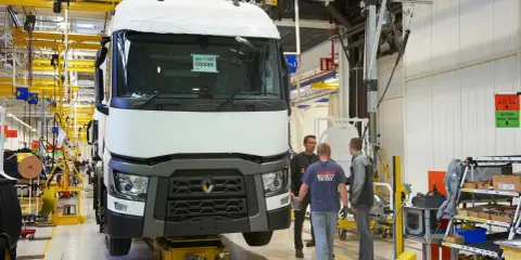 Tres trabajadores observan un camión Renault en una línea de montaje. El camión está sobre una plataforma amarilla.