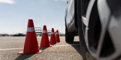 Conos naranjas marcan la zona f para el carnet C. Un coche se acerca, listo para la maniobra.