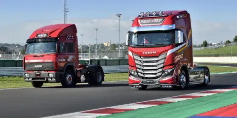 Dos camiones Iveco rojos, uno antiguo y otro moderno, en una pista de carreras.