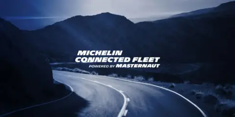 Carretera sinuosa bajo un cielo azul oscuro, con el texto "MICHELIN CONNECTED FLEET" iluminado.