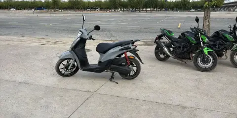 Un carnet scooter gris y dos motos verdes aparcadas en un circuito.
