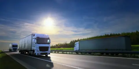 Camiones blancos circulan por la autopista bajo un cielo azul y soleado. El carnet TIR es esencial para estos transportes.