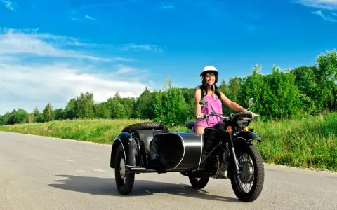 Mujer sonriente con casco blanco conduce una motocicleta negra con sidecar. El permiso A1 autoriza a conducir motocicletas con sidecar.