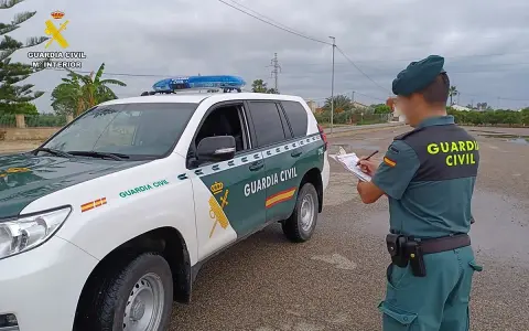Agente de la Guardia Civil anota datos junto a un vehículo oficial. Se pregunta qué carnet se necesita para conducir un minibus.