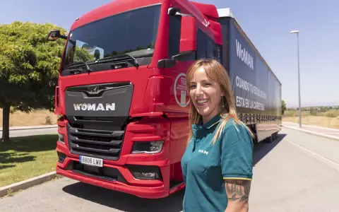 Mujer sonriente junto a un camión rojo MAN TGX. Averigua cuanto cuesta el carnet C+E para conducir este vehículo.