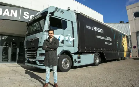 Hombre posa frente a un camión eléctrico MAN, como en las revistas de camiones. El remolque tiene un león y el lema "Construimos el futuro".