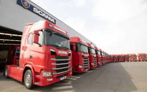 Una fila de camiones Scania rojos, listos para la acción, con el logo de Scania en el edificio.