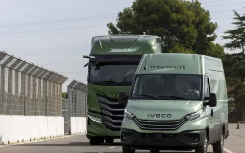 Dos vehículos Iveco, un camión y una furgoneta, ambos de color verde y con la etiqueta "DEMO VEHICLE", circulan por una carretera.