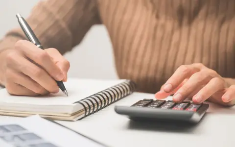 Calculando el precio de clases de conducir. Mano con bolígrafo en cuaderno y otra mano en calculadora.