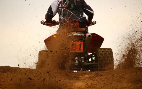 Un quad naranja con el número 1 salpica barro a máxima velocidad.