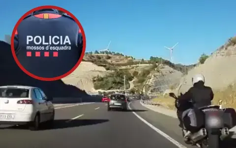 Un motorista de los Mossos d'Esquadra circula por el arcén de una autopista, adelantando a otros vehículos en un día soleado.