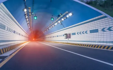 El efecto túnel se percibe al entrar en este túnel vial iluminado, con luces verdes y un resplandor rojo al fondo.