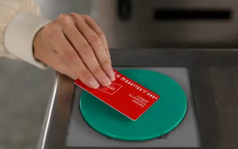 Mano acercando tarjeta roja de transporte público a un lector verde.
