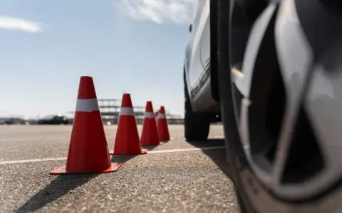 Conos naranjas marcan la zona f para el carnet C. Un coche se acerca, listo para la maniobra.