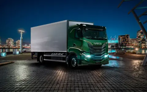 Camión Iveco S-Way V8 780 verde brillante aparcado en un muelle urbano de noche, con luces de ciudad al fondo.