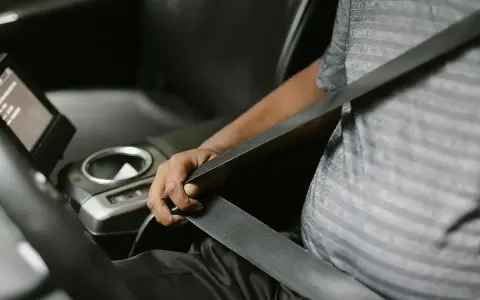 Persona se abrocha el cinturón de seguridad en un coche moderno. Las normativas de tráfico exigen que todos los pasajeros, a menos que estén exentos de llevar cinturón de seguridad, lo usen.