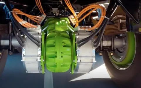 Detalle del sistema de freno eléctrico de camiones, con componentes verdes y naranjas, y cables negros.