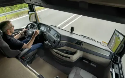 Conductor en un camión moderno sin retrovisores, usando pantallas digitales para ver el camino.