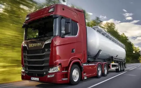 Camión cisterna Scania 800 CV de color rojo brillante, circulando por una carretera rodeada de árboles.