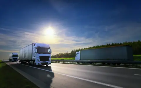 Camiones blancos circulan por la autopista bajo un cielo azul y soleado. El carnet TIR es esencial para estos transportes.