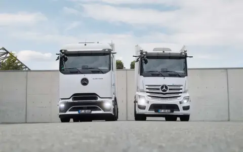 Dos camiones Mercedes-Benz eActros blancos, un nuevo camión eléctrico, se exhiben frente a un muro de hormigón.
