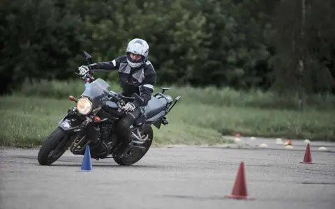 Persona con casco y equipación de moto practica maniobras en circuito con conos. Averigua el carnet de moto a1 precio.