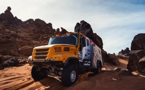 Camión Iveco Dakar amarillo compitiendo en un terreno desértico rocoso y arenoso, levantando polvo.