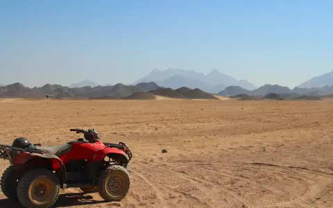Un quad rojo, listo para la aventura, descansa en el desierto. El carnet para conducir quad 660 es tu pase a la emoción. Montañas distantes y cielo azul completan la escena.