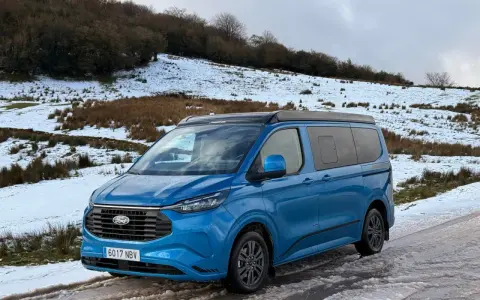 Furgoneta phev azul aparcada en un camino nevado, lista para una aventura invernal.