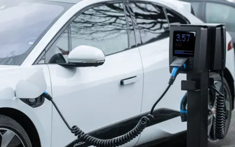 Coche eléctrico blanco cargando. El poste de carga muestra 3.57 kW, cumpliendo el reglamento AFIR para la infraestructura de energía.