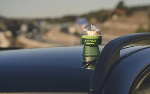 Baliza LED verde y plateada, modelo LEDONE CONNECTED, sobre el techo de un coche. Es una preseñalización de peligro para advertir en carretera.