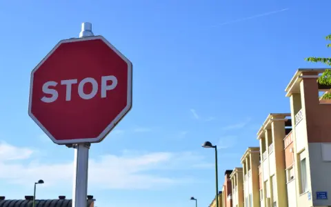 Señal de STOP roja en un poste, con edificios y cielo azul. Indica cómo hacer un stop sin visibilidad.