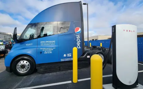 Camión semirremolque azul Pepsi junto a un cargador Tesla.