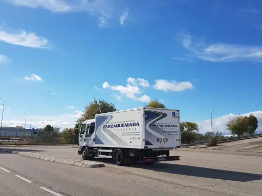 Camión de autoescuela Zarzaquemada, listo para obtener el carnet C+E. Cielo azul con nubes.
