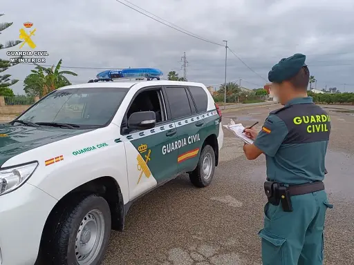 Agente de la Guardia Civil anota datos junto a un vehículo oficial. Se pregunta qué carnet se necesita para conducir un minibus.
