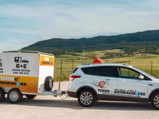 Un coche blanco de **4x4 autoescuela** con remolque, listo para enseñar a conducir en un paisaje rural.