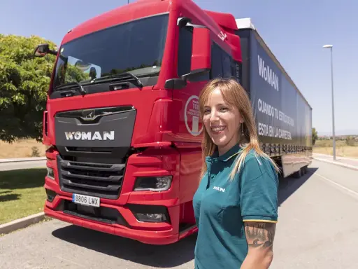 Mujer sonriente junto a un camión rojo MAN TGX. Averigua cuanto cuesta el carnet C+E para conducir este vehículo.
