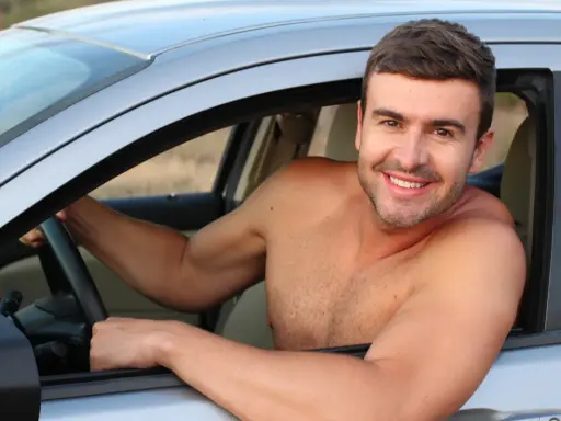 Hombre sonriente al volante de un coche, disfrutando de la libertad de que se puede conducir sin camiseta en un día caluroso.